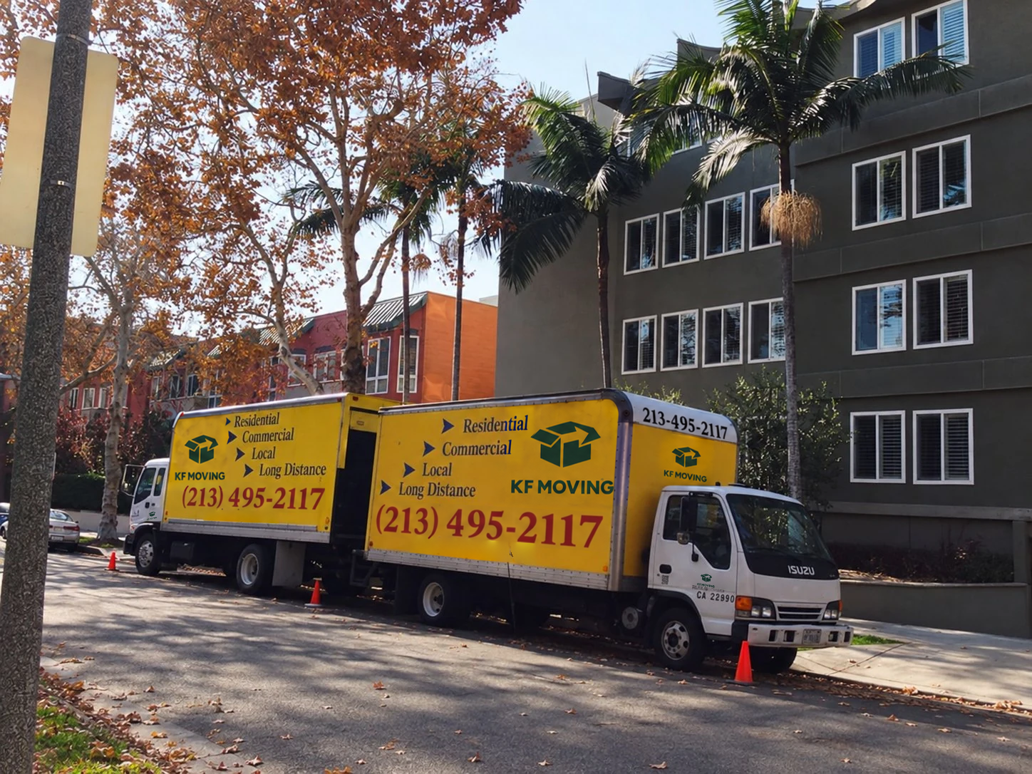 Two yellow KF Moving trucks parked outside an apartment building